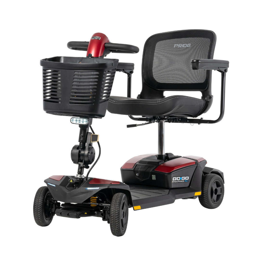 The Pride Mobility Go Go® Endurance AL+ Power Scooter is a red and black four-wheel scooter with a mesh backrest, front basket, and easy-to-use grid-style controls, designed for personal transportation and assisted mobility.